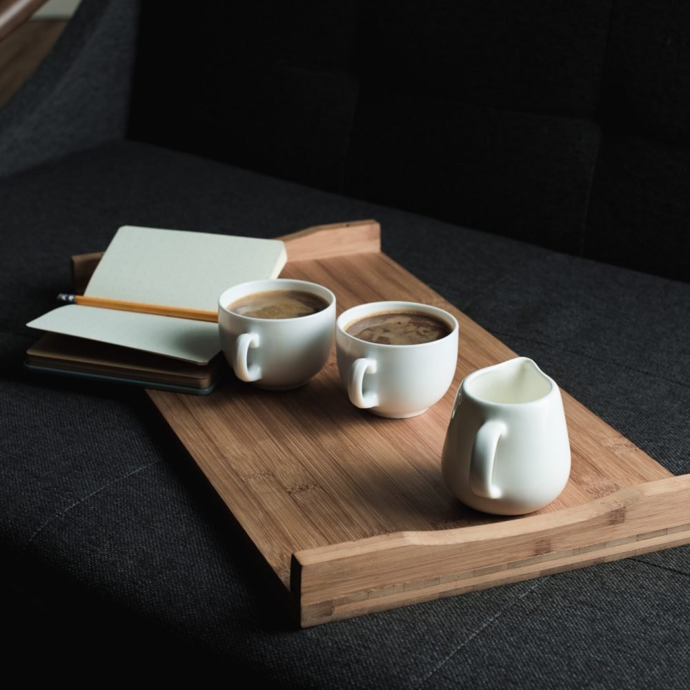 two-cups-of-coffee-jug-of-milk-and-notebook-with-pencil-on-wooden-tray-on-sofa-2